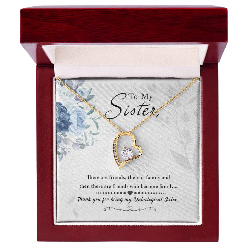 Yellow Gold Forever Love Heart Necklace. Large CZ crystal at center with small crystals along one side. Shown in Luxury Gift Box. Message reads:To My Sister: There are friends, there is family, and then there are friends who become family... thank you for being my unbiological sister. There are blue flowers in the background.