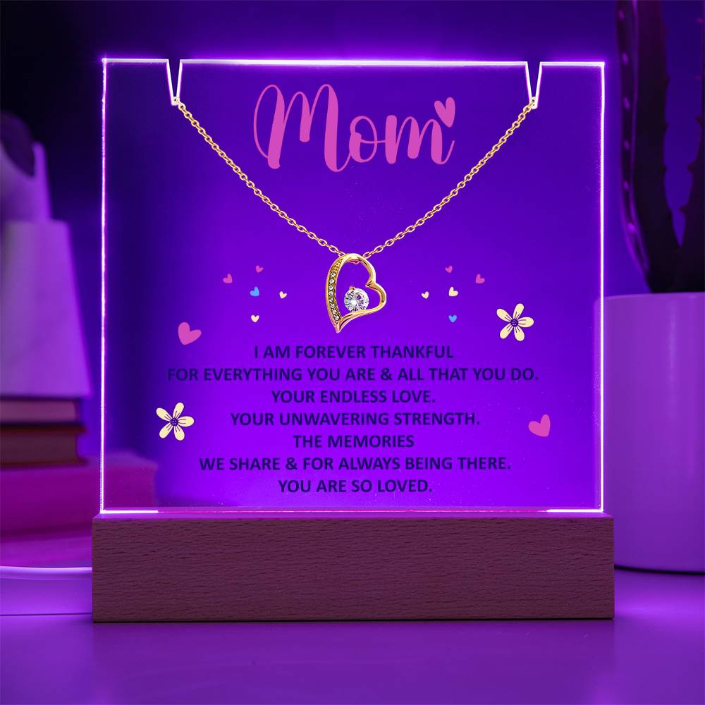 Clear Acrylic Plaque with the saying Mom - I am forever thankful for everything you are and all that you do. Your endless love. Your unwavering strength. the memories we share and for always being there. You are so loved. (Corded base, purple led light illuminated, color can be adjusted) There are two notches in the top of the plaque where the forever heart necklace is placed. 18K yellow gold plated heart, with a large single cubic zurconia in the center and several smaller stones on one side.